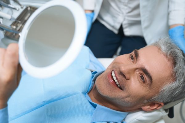 man with gray hair looks at smile in mirror