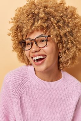 woman with curly hair wearing glasses smiles